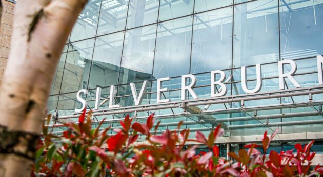 A photo of the glass entrance to Silverburn, with autumnal leaves in the foreground and the white Silverburn lettering in the background,