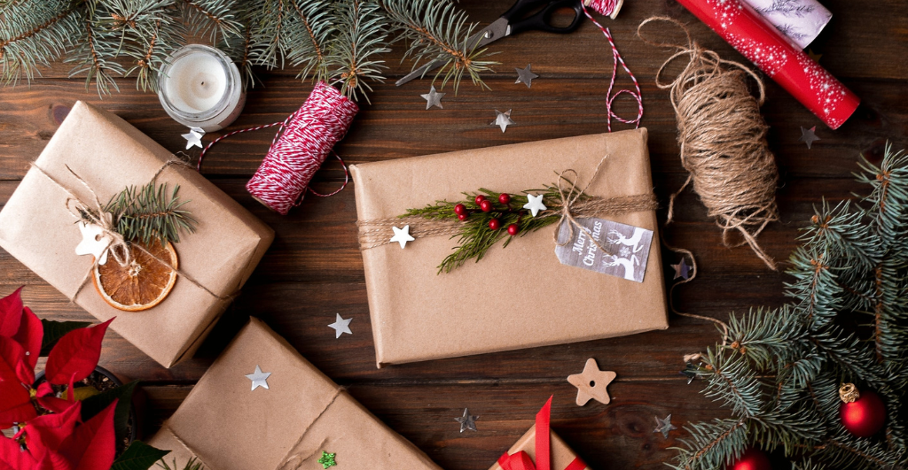 Spread the cost of Christmas with homemade gifts - Birds eye view of Christmas presents laid out on a wooden floor, wrapped up with brown paper, twine, fresh branches and dried fruit.