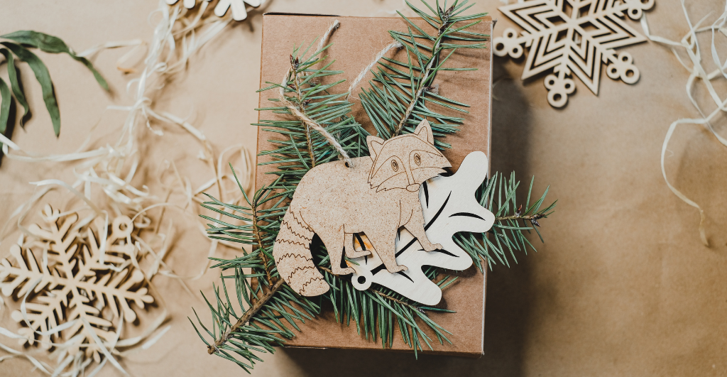 Eco friendly christmas - top down view of wooden raccoon bauble with pine needles and wooden snowflake baubles on a brown paper background