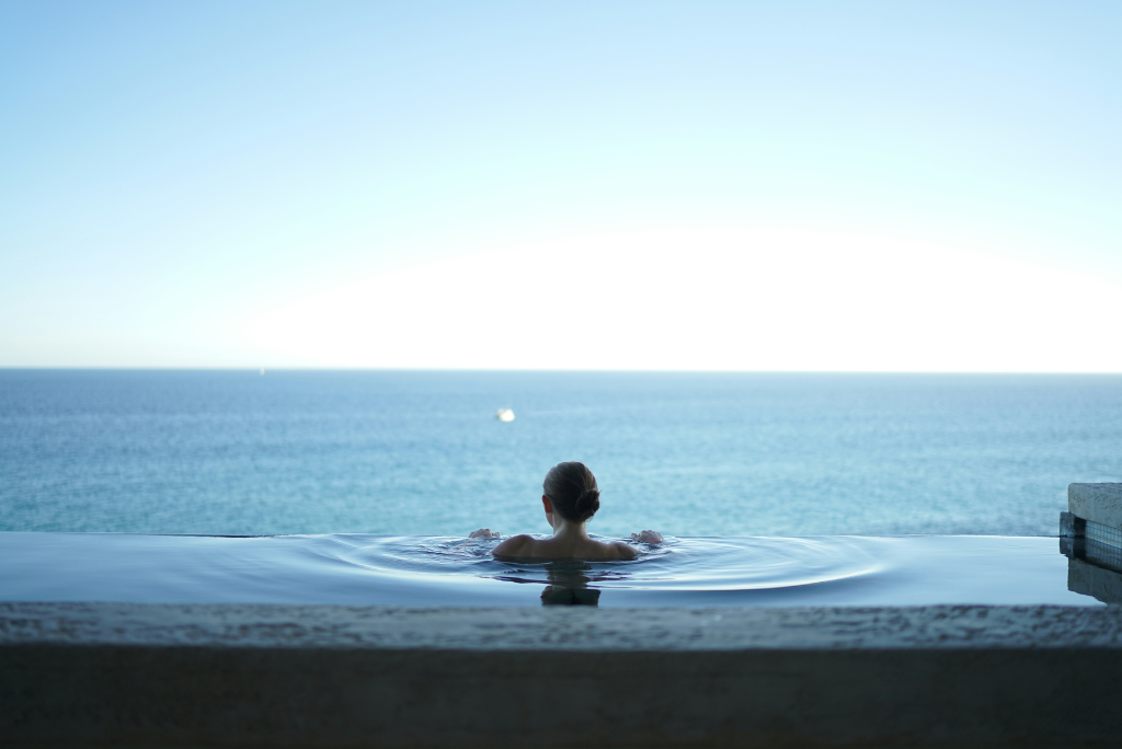 Woman relaxing in an infinity pool looking over the ocean